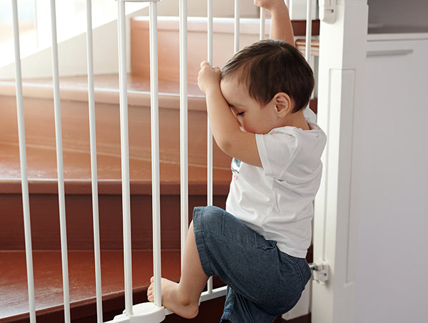 Baby trying to climb a baby gate blocking the stairs