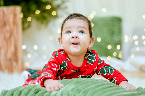 Baby in red and green Christmas tree onesie exploring their surroundings