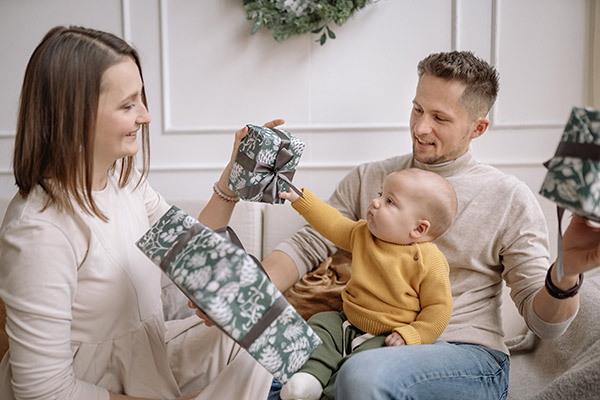 Baby pulling on a Christmas present's ribbon while sitting on father's lap