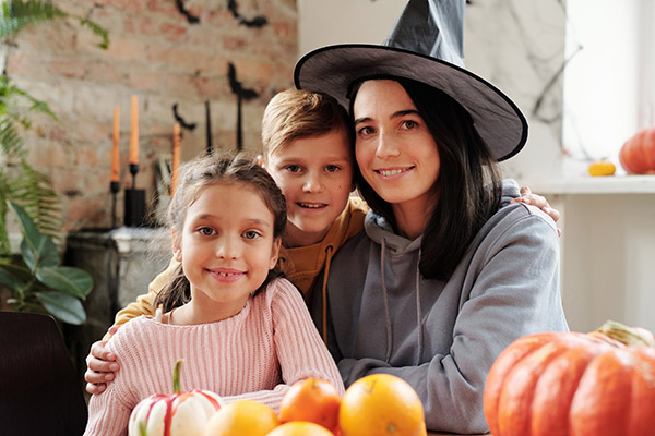 Family posed with pumpkins, mother in a witch hat hugging her son and daughter