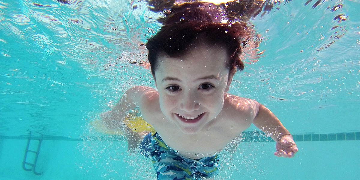 Young Smiling Boy Swimming Underwater in a Pool