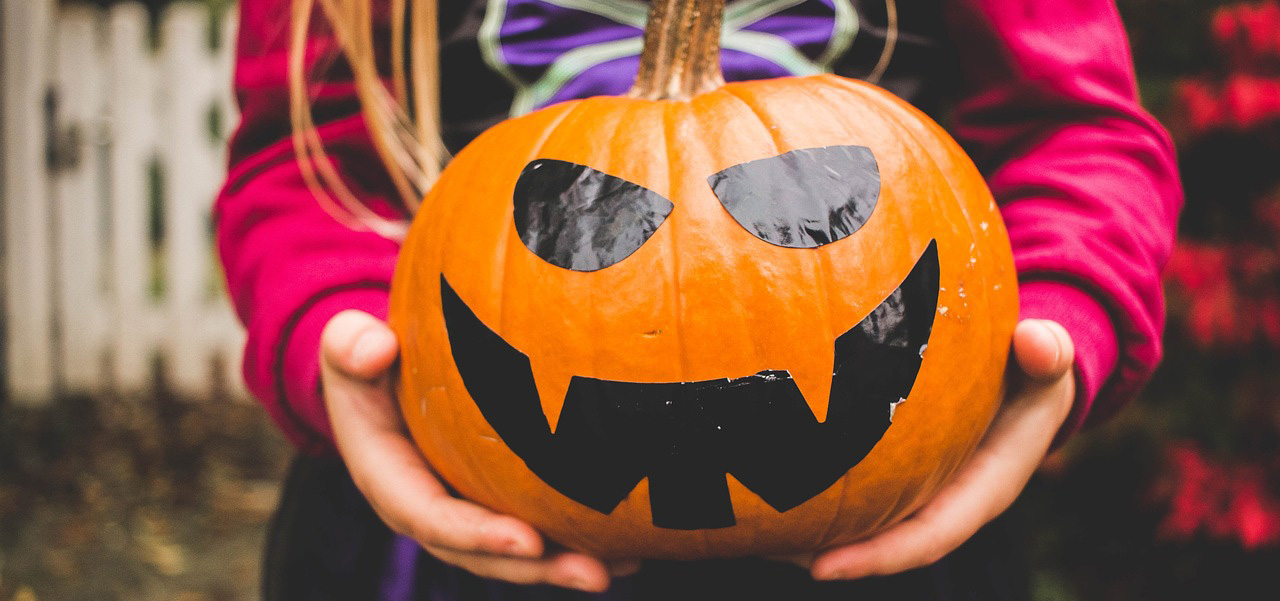 Brightly costumed trick-or-treater holding a painted pumpkin in their hands