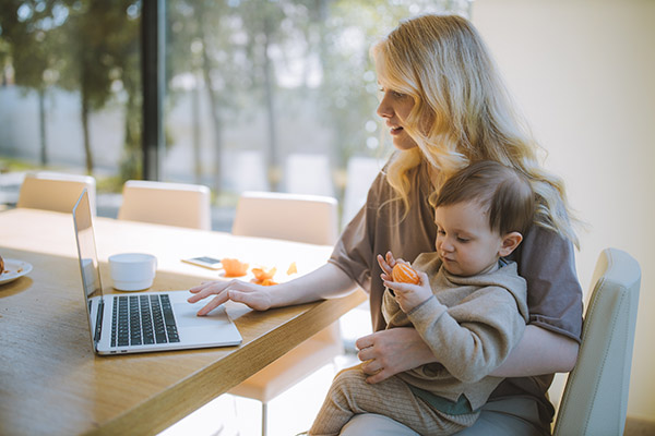 Woman with toddler video chatting to stay in touch; sitting with laptop at kitchen table