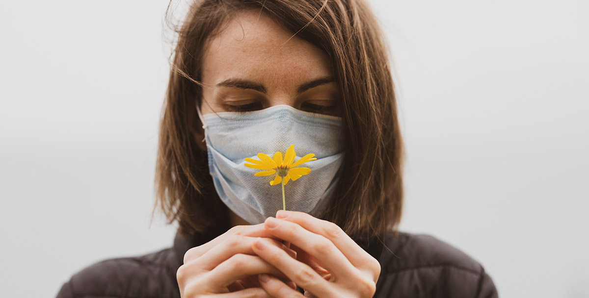 Woman in mask holding yellow flower up to her nose | Pexels-engin-akyurt