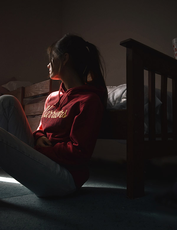 Young woman sitting on the floor of her college dorm in shadow (Image Source Pexels)