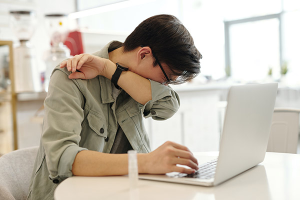 Young man on laptop stopping to sneeze into the crook of his elbow