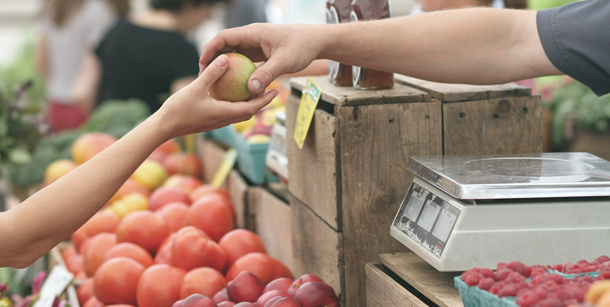 Person purchasing an apple at a farmer's market full of seasonal produce