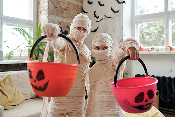 Two children dressed as mummies with Halloween trick-or-treat candy pails