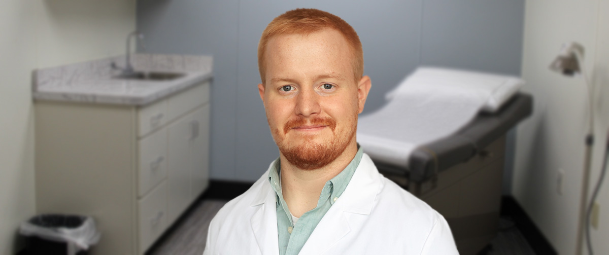 Photo of Spencer Castle, certified registered nurse practitioner. in an exam room wearing his white coat; he now provides family medicine healthcare at Mansfield Laurel Health Center, located at 416 South Main Street in Mansfield, PA