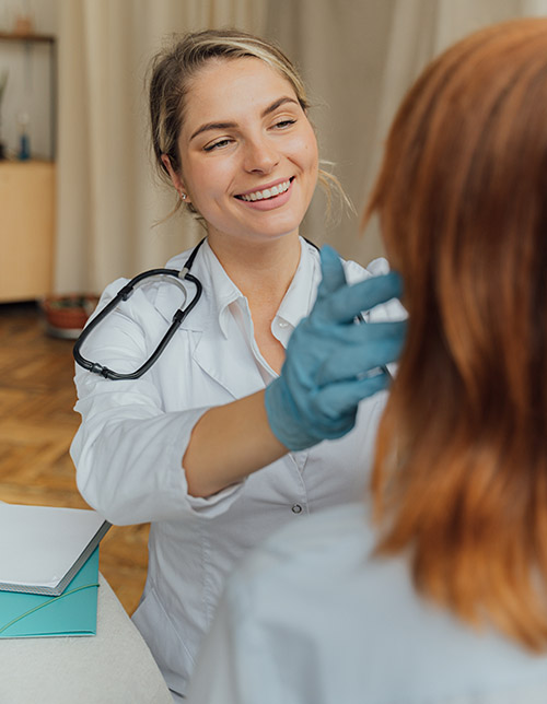 Smiling female healthcare provider in a white coat examining a patient's neck