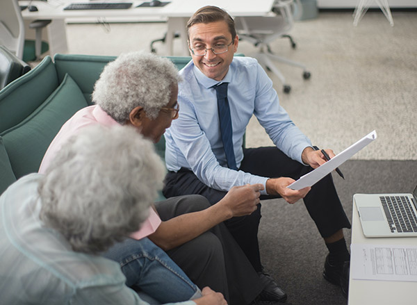 Smiling Man in Glasses Helping Older Couple with Enrollment Paperwork; Photo by Krampus Productions