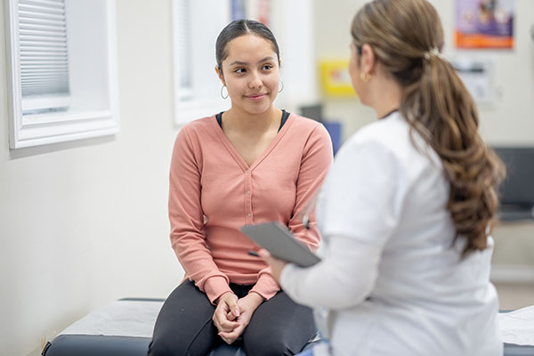 Young woman seated on an exam table discussing wellness with her healthcare provider
