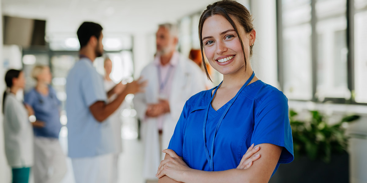 Smiling nurse in blue scrubs standing in doctor's office; Laurel Health is sponsoring local students to pursue nursing and dental careers