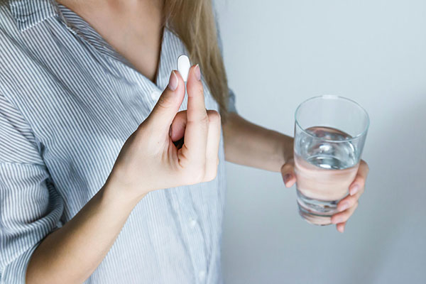 Blond woman talking an allergy pill with a glass of water