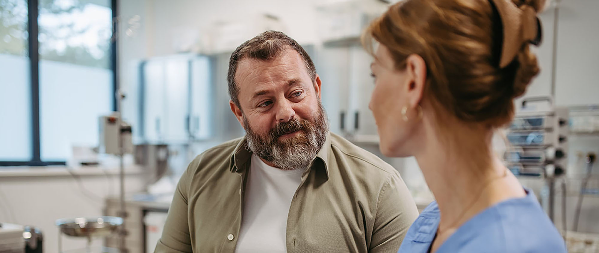A middle-aged male patient talks with a nurse about his diabetes symptoms in a medical office exam room.
