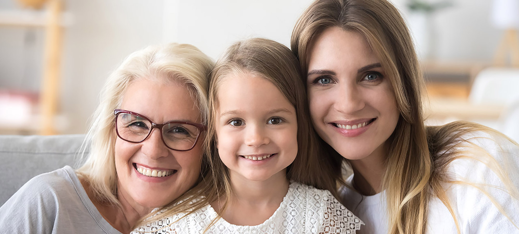A daughter, mother, and grandmother smile into the camera representing three generations of one family.