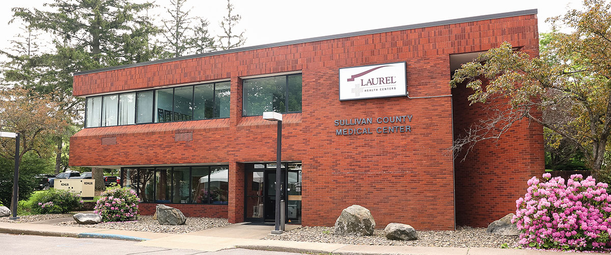 Sullivan County Laurel Health Center; it is a two-story brick building flocked by trees and landscaped garden beds.